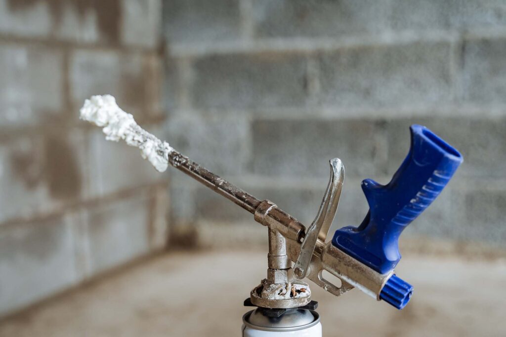 Foam gun with blue handle, spraying insulation.